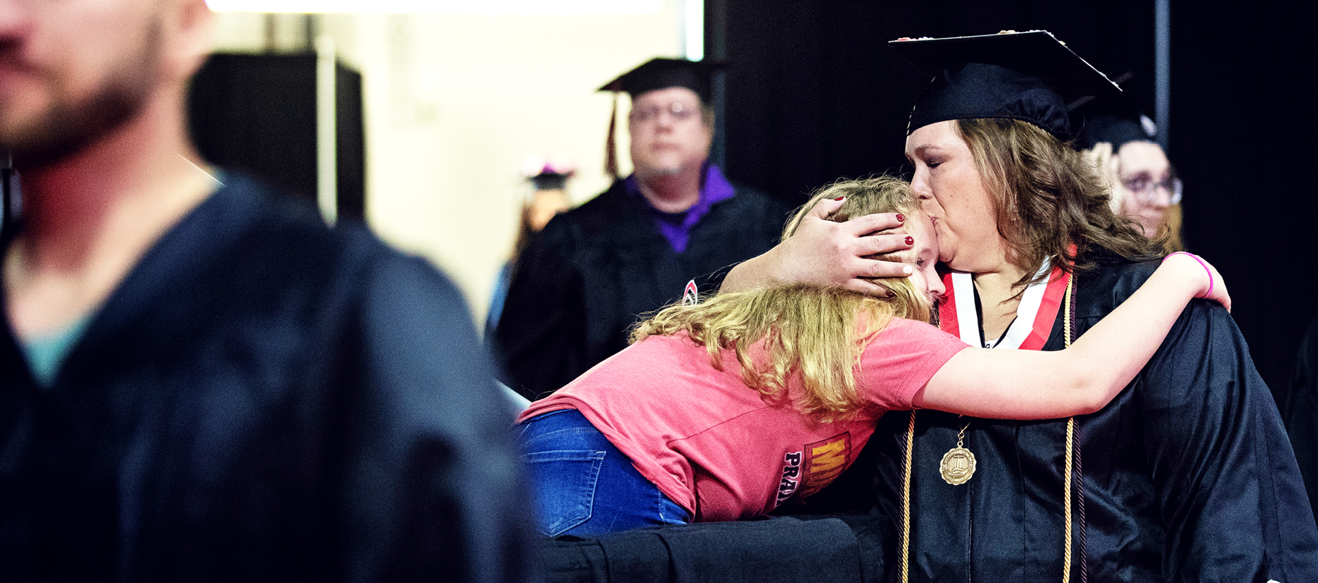 a graduating mom hugs and kisses her daughter at commencement