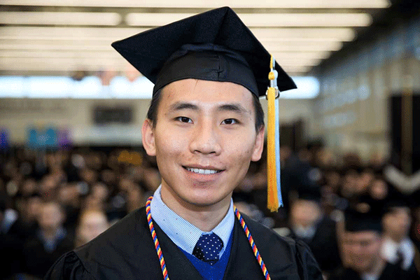 a student in graduation gear smiles at the camera.