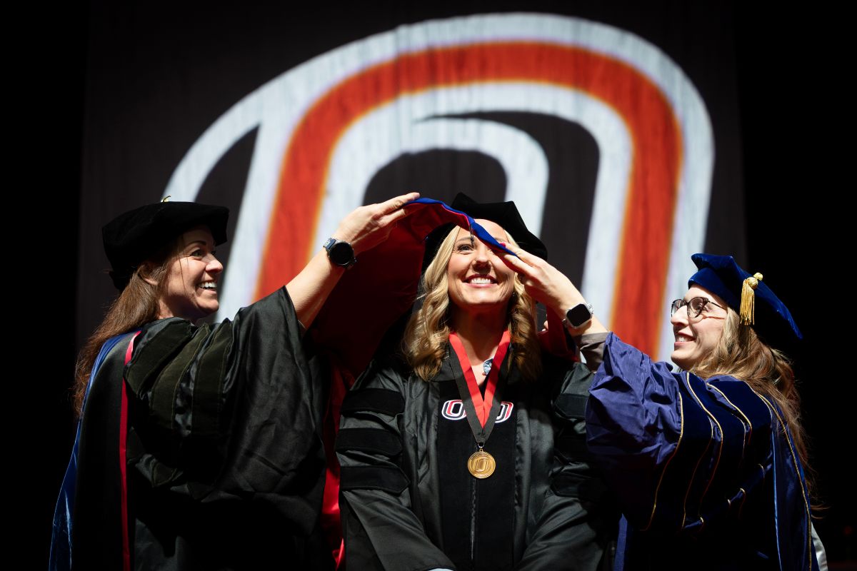Graduate student being hooded at graduation by dean and associate dean.