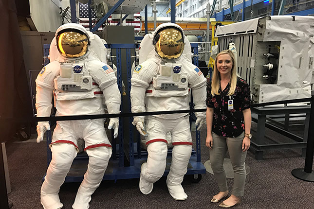 Sandra Jones posing in front of space suits.