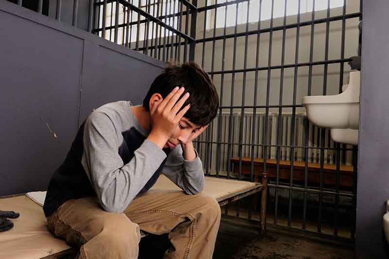 Teenager sitting in a jail cell.