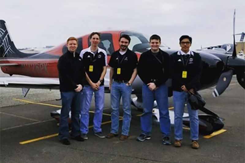 Alpha Eta Rho members posing in front of a plane