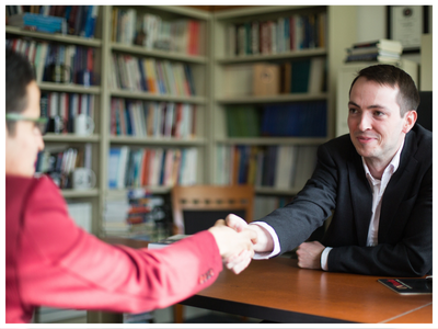 Two men sitting at a desk and shaking hands.