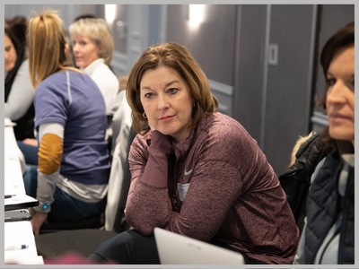 Woman sitting at a table with others listening to a speaker.