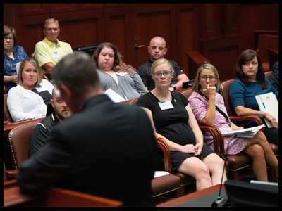 Group of people sitting in a courtroom listening to a speaker.