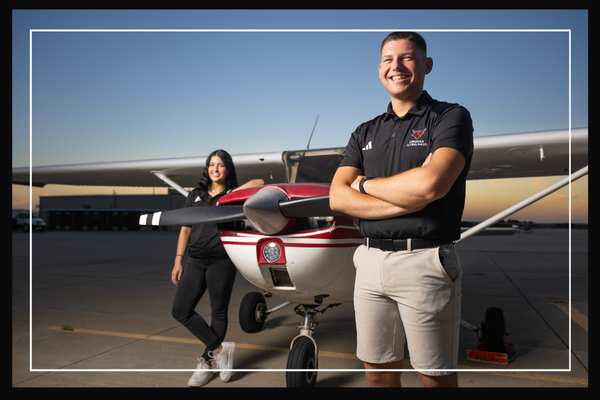 two students standing in front of an airplane.