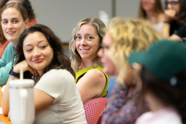 a woman loks directly at the camera and smiles while sitting in class.