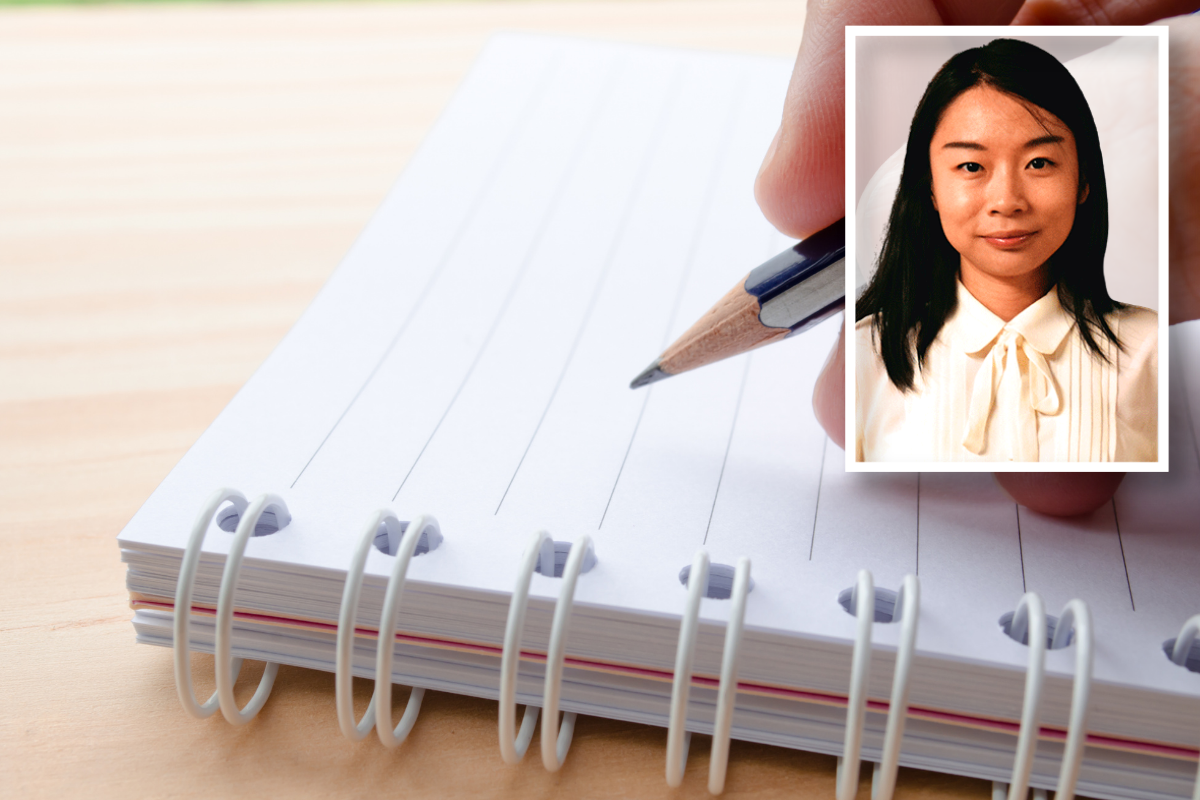 Hand holding a pencil and writing in a notebook.