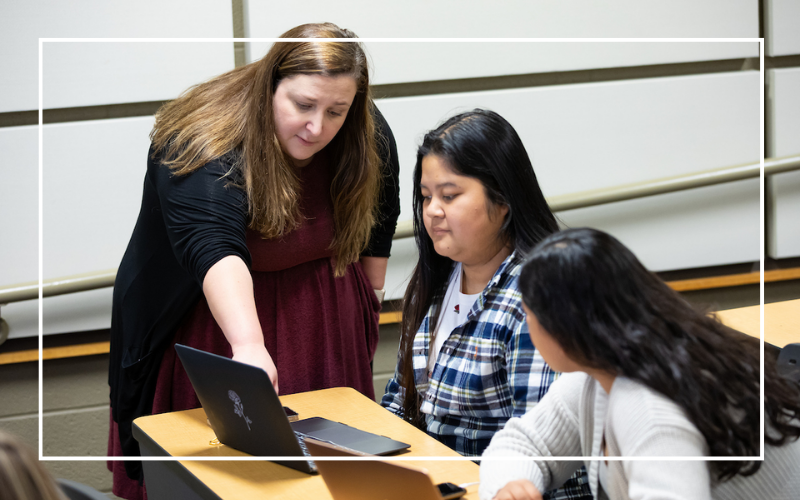 Instructor pointing at something on a laptop in front of two students.