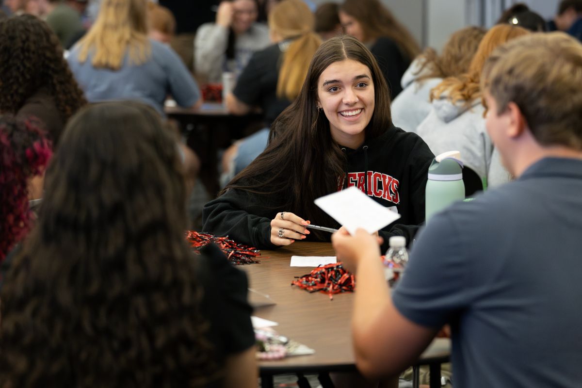 Students talking and sitting in a classroom at a table full of swag.