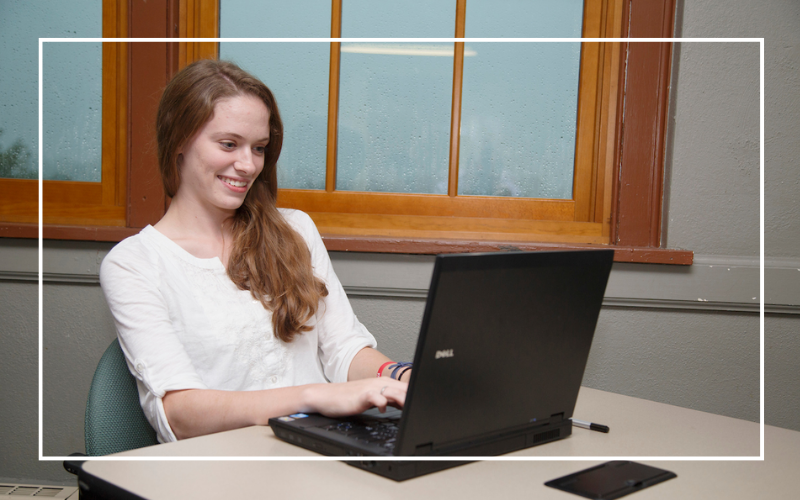 Student sitting in front of a window, typing on a laptop.