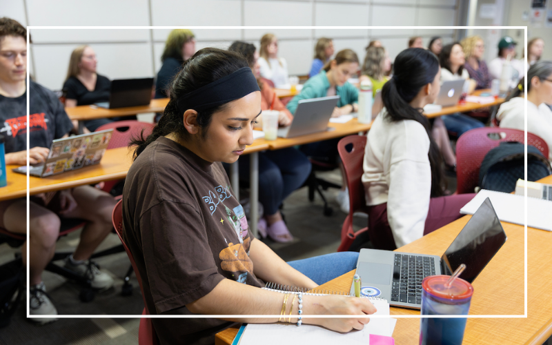 Student in classroom with other students writing in a notebook.