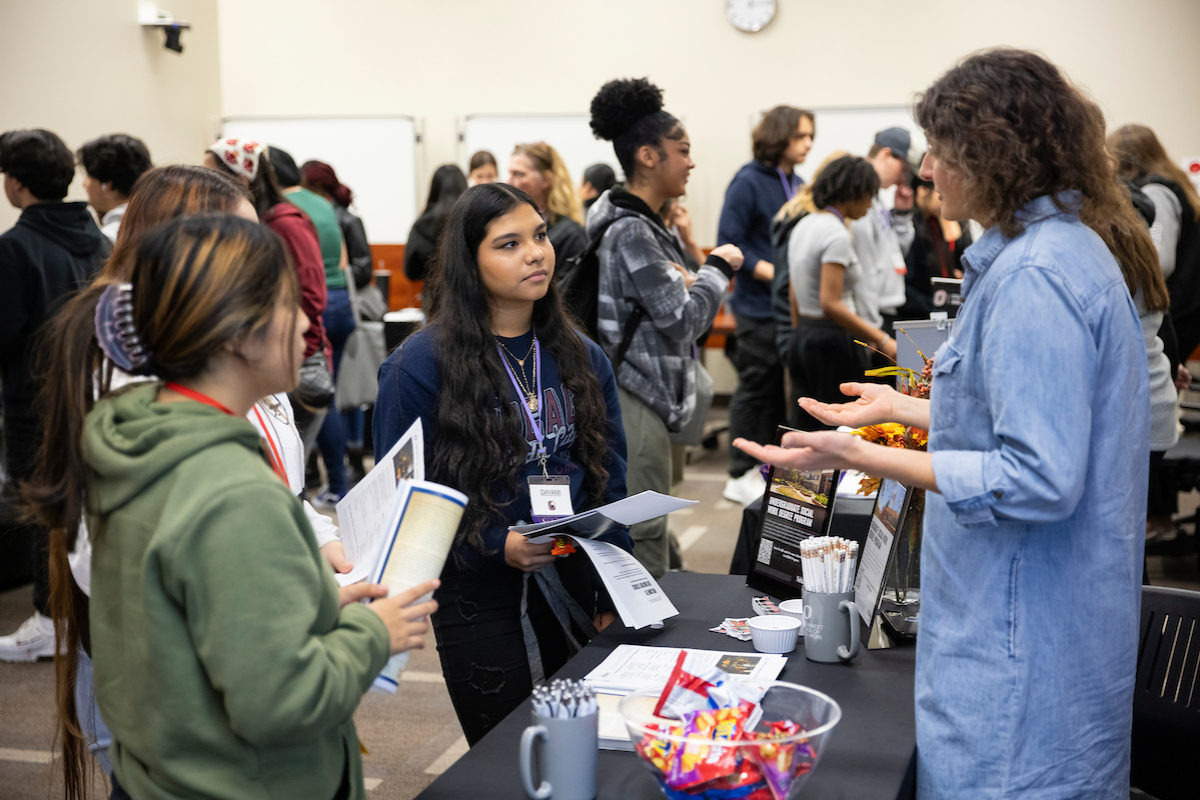 Multiple students talking to an advisor standing behind a table with marketing materials.