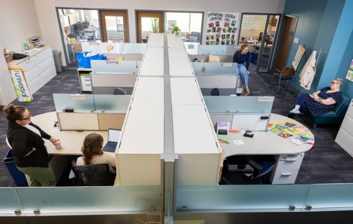 Overhead view of semi-private cubicles with several staff members working and meeting in an open office layout.