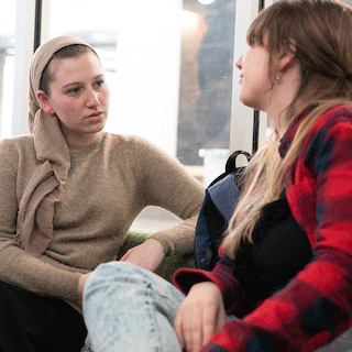 Two students seated indoors, engaged in a thoughtful one-on-one conversation in a comfortable campus space.