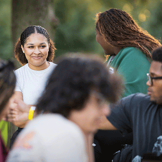 Students gathered outdoors on campus, smiling and talking together in a relaxed, supportive setting.