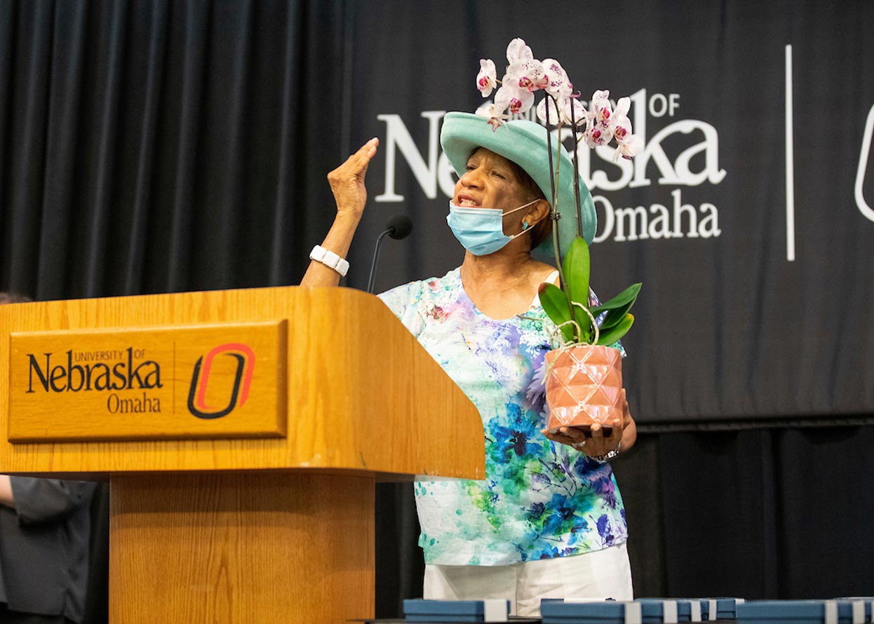a member of the omaha 54 speaking at the podium, she is holding a plant