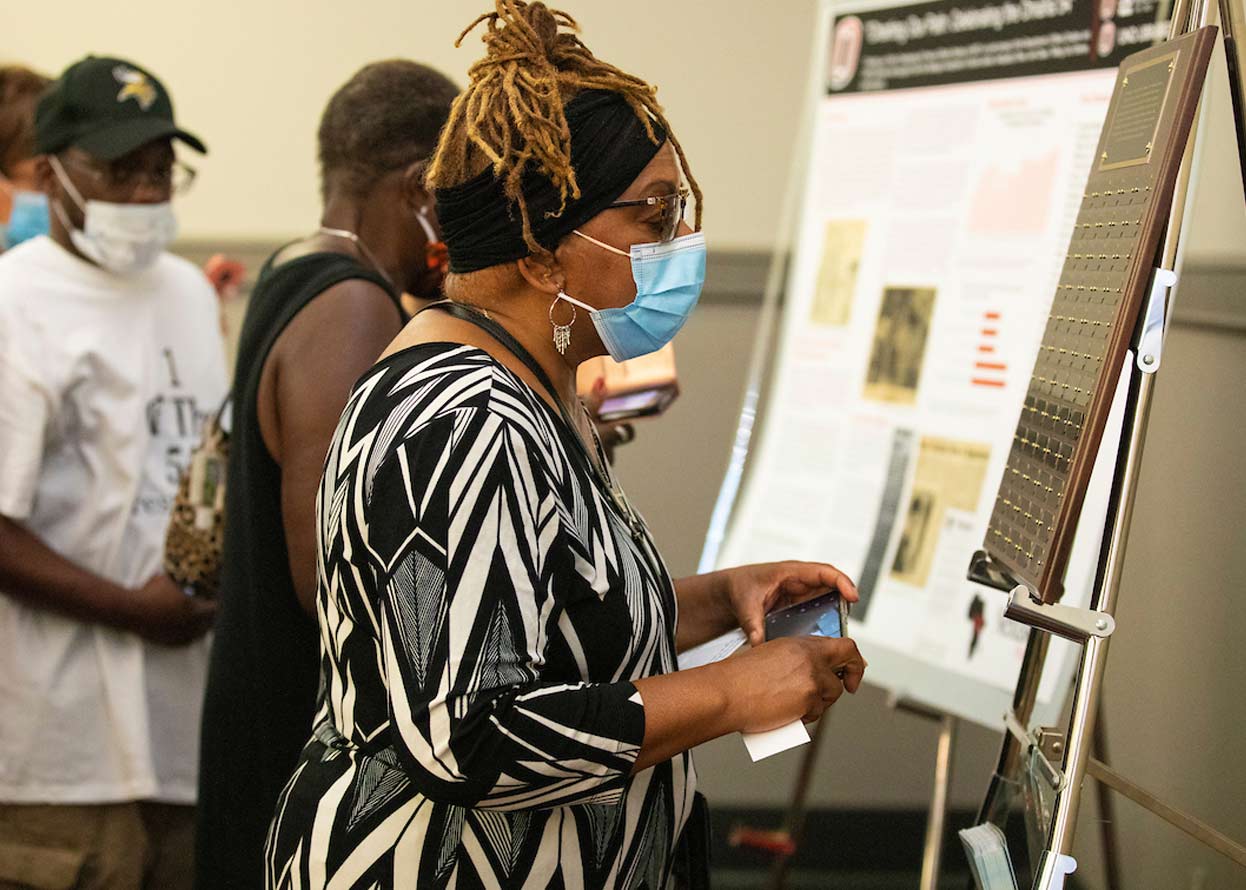 a woman with a mask on looking at a plaque with names on it 