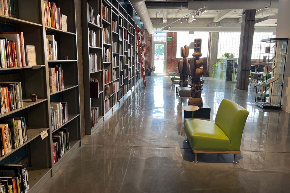 a row of green couches situated to view bookshelves with statues near the couches