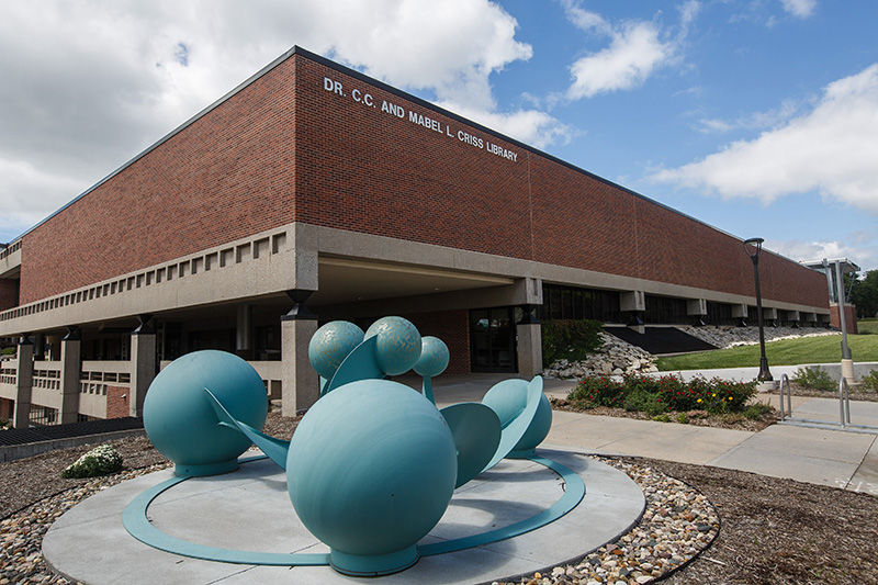 the criss library building in the background, and in the foreground a blue, multi-sphere scuplture