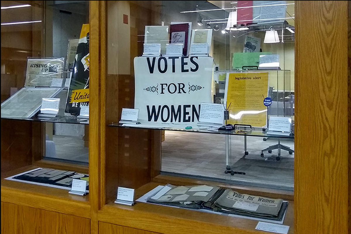 banner that says 'votes for women' within display cases 