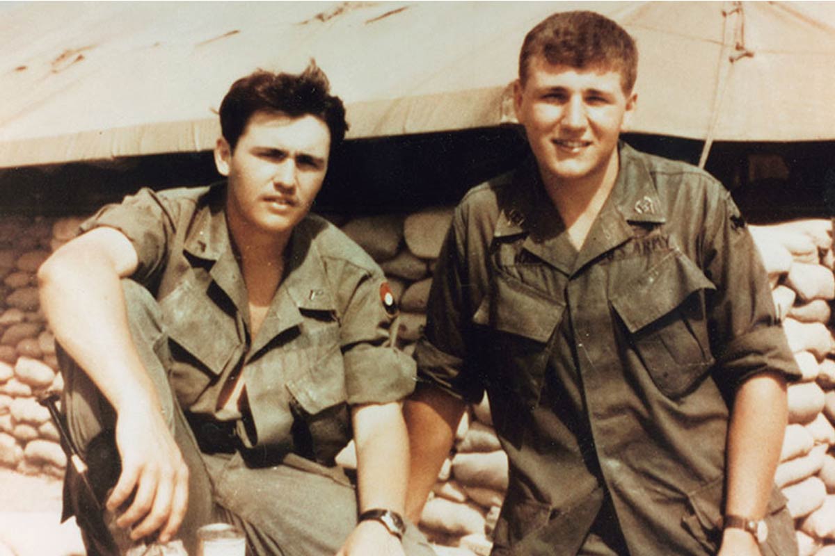 two men in army uniforms sitting in front of a tent