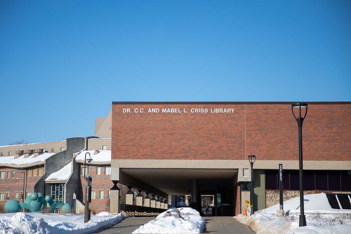 a brick building with the words 'Criss Library', snow piles are on the ground around the building but the walkway is clear 