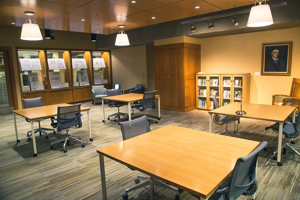 a library archive reading room with tables and chairs in the room, a small bookshelf, and built in glass and wood shelves