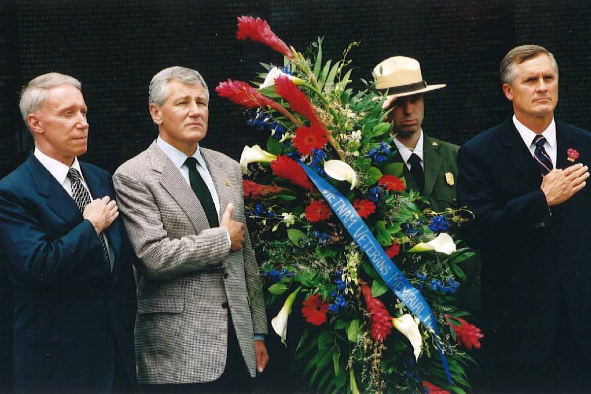 four men with their hands on their hearts standing behind a floral arrangement