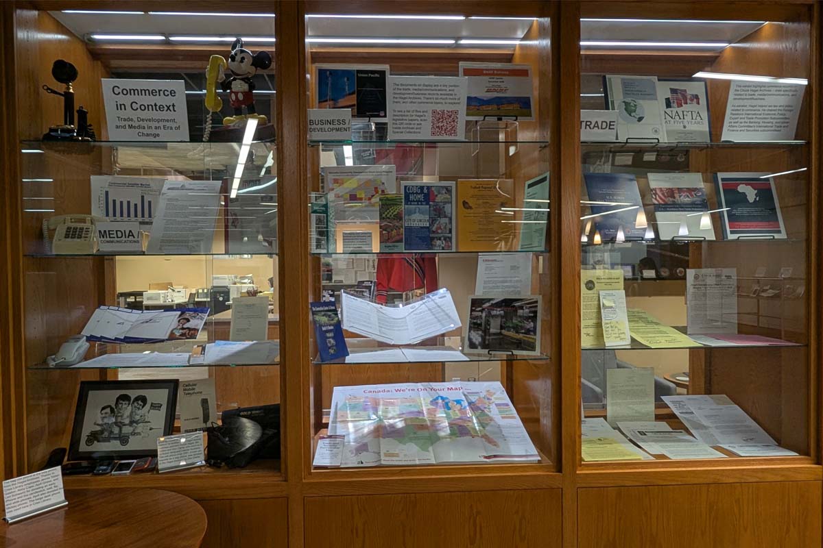 A wooden display case with glass shelves featuring items related to commerce, including documents, brochures, and a Mickey Mouse phone..