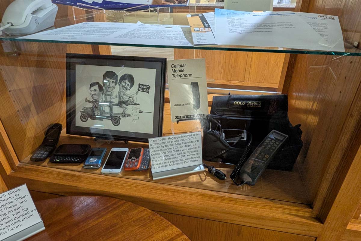 Display case with historical mobile phones, framed cartoon, and a "GOLD SERIES by Motorola" phone in a carry case.