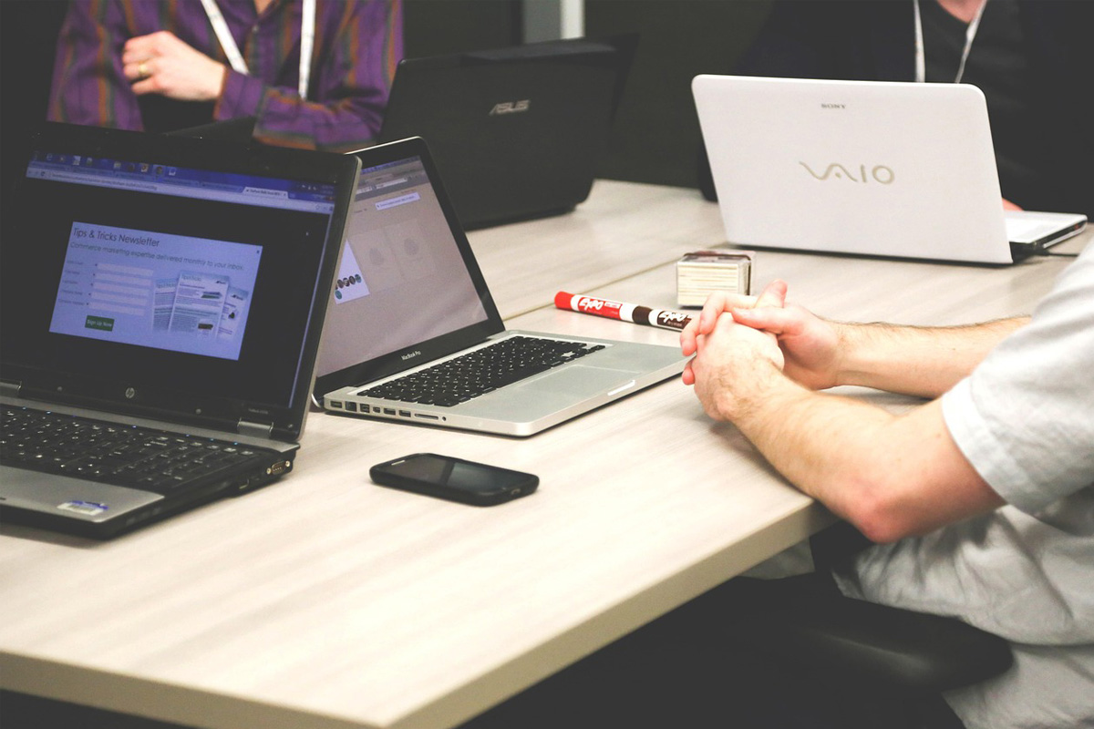 Laptops on a conference table with a smartphone and a person with clasped hands.