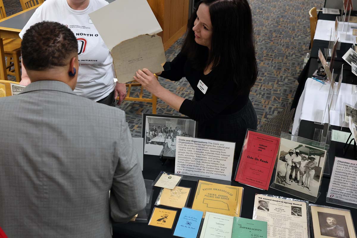 Woman showing an old document to a man at a table displaying historical materials.