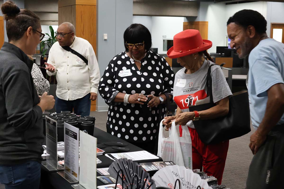 People interacting at a display table with promotional items at an indoor event.