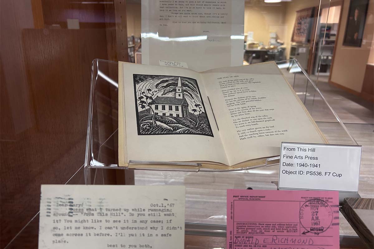 A display case with an open book featuring a church illustration and poem, alongside typed correspondence and labels.