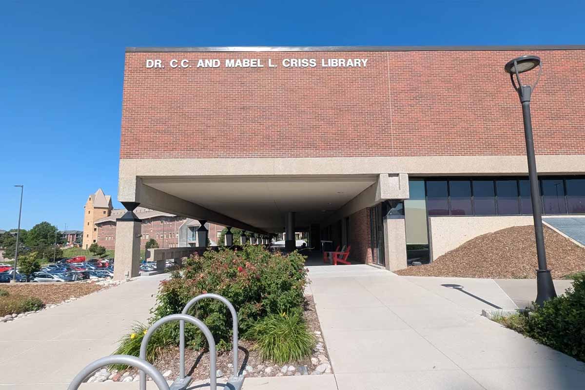 A walkway going under a brick building. The building says 'Dr. C.C. and Mabel L. Criss Library' on the outside. There is a bike rack and foliage near the building.