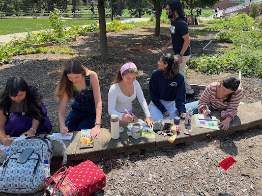 5 girls painting small wooden signs in the gardens, the signs show fruits or vegetables that will be grown
