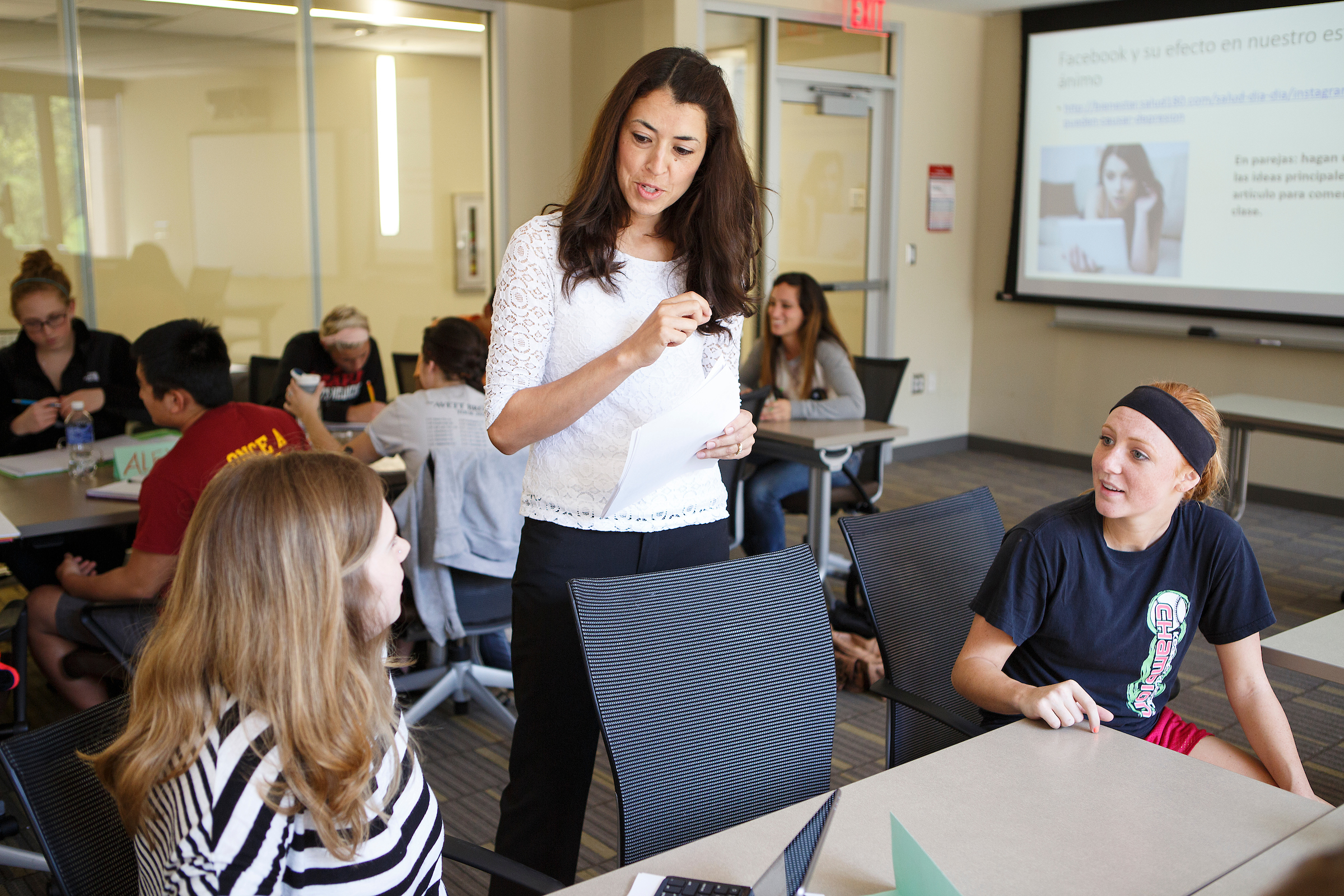 Instructor talks with two students at a table in a Spanish class.