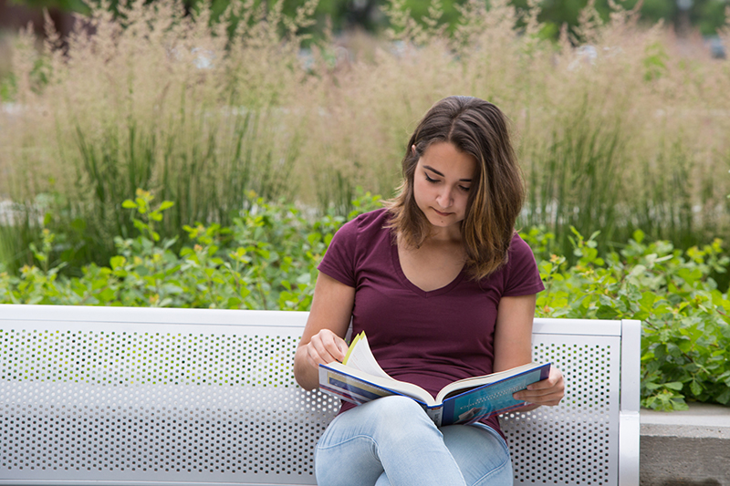 Student sitting on bench, reading textbook.