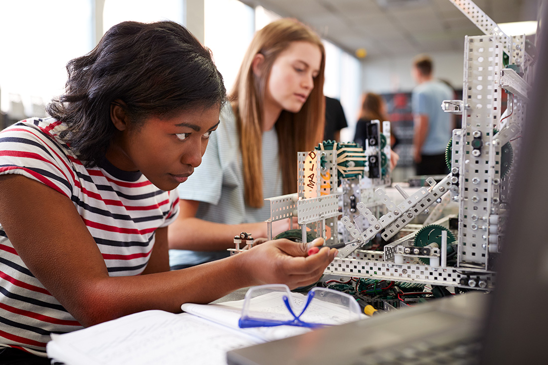two students working on machine in high school science classroom.