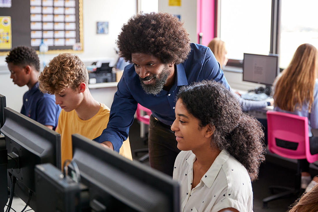 smiling teacher overseeing students while they work in computer lab.