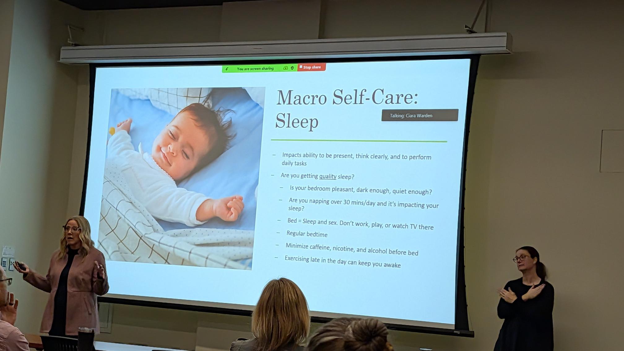 Presenter Ciara Warden stands in front of her presentation slide. A sign language interpreter interprets to the left.