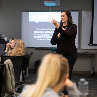 A woman presents to a seated group in a classroom.