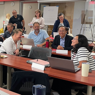 A group of faculty sit at tables while talking and smiling.