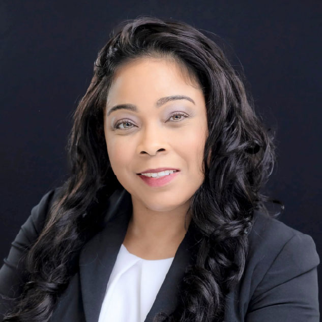 Professional woman with long wavy black hair wearing a black blazer over a white top, smiling gently in front of a solid black background.