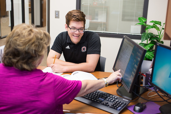 A student gets advising help as he sits at a desk with a U-N-O staff member.