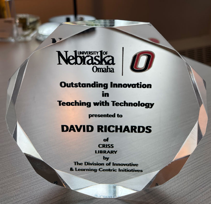 Crystal award with beveled edges presented by the University of Nebraska Omaha. The text on the award reads: "Outstanding Innovation in Teaching with Technology presented to David Richards of Criss Library by The Division of Innovative & Learning Centric Initiatives." The university logo and UNO athletic 'O' symbol are engraved at the top.