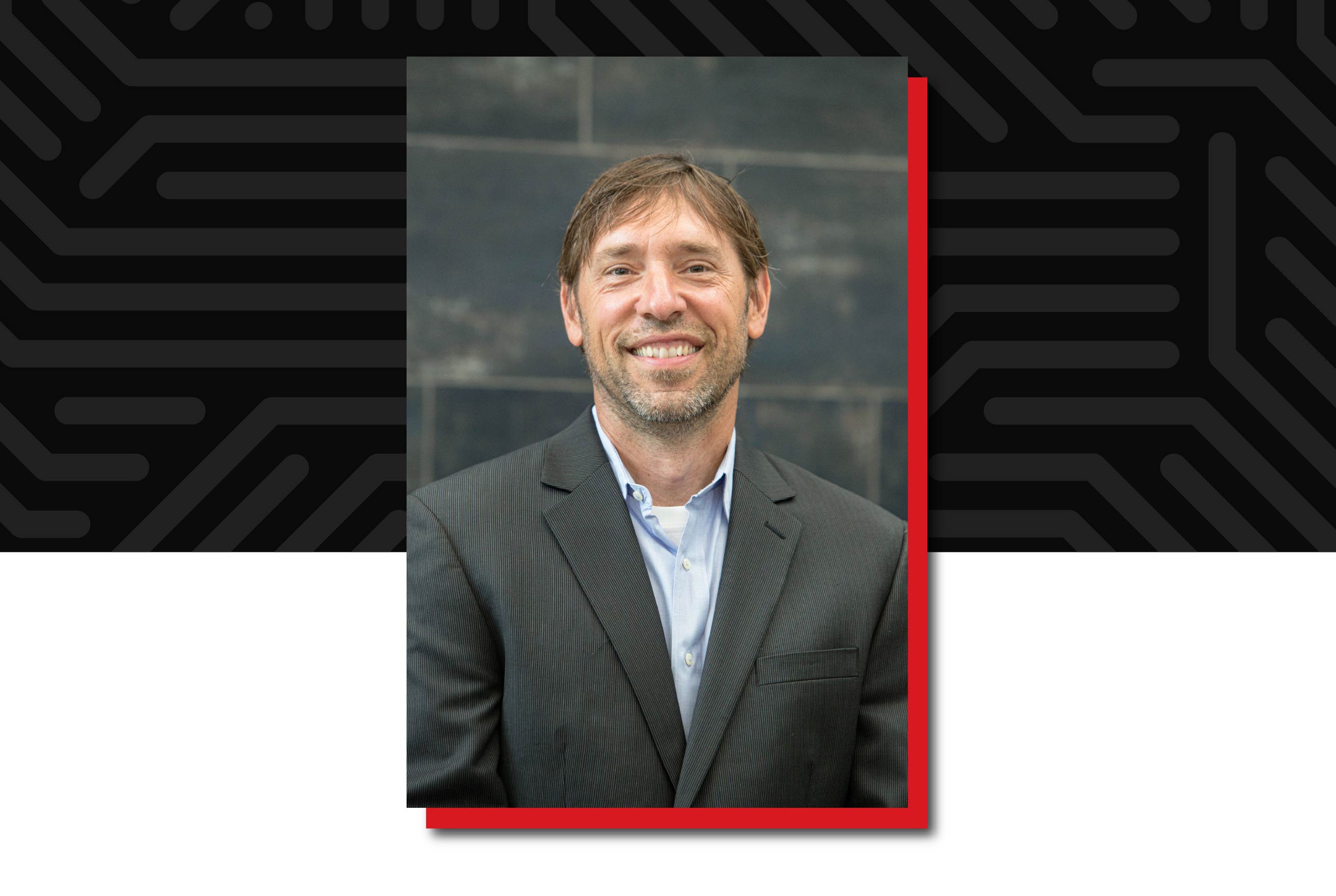 Craig Maher, professor in the School of Public Administration, smiles while wearing a dark blazer and light blue shirt against a dark background.