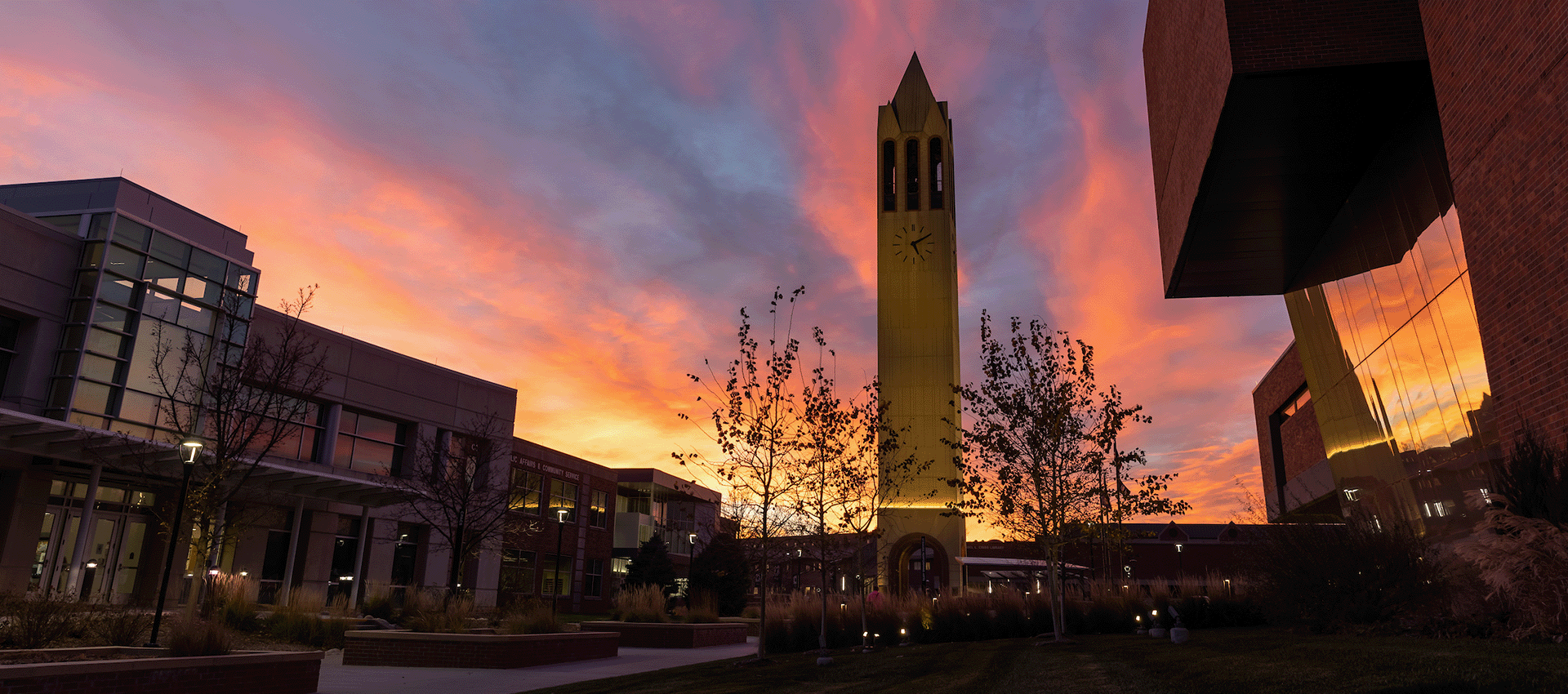 The University of Nebraska at Omaha campus, center-image is the Henningson Memorial Campanile set with a orange, blue, and yellow sunset.