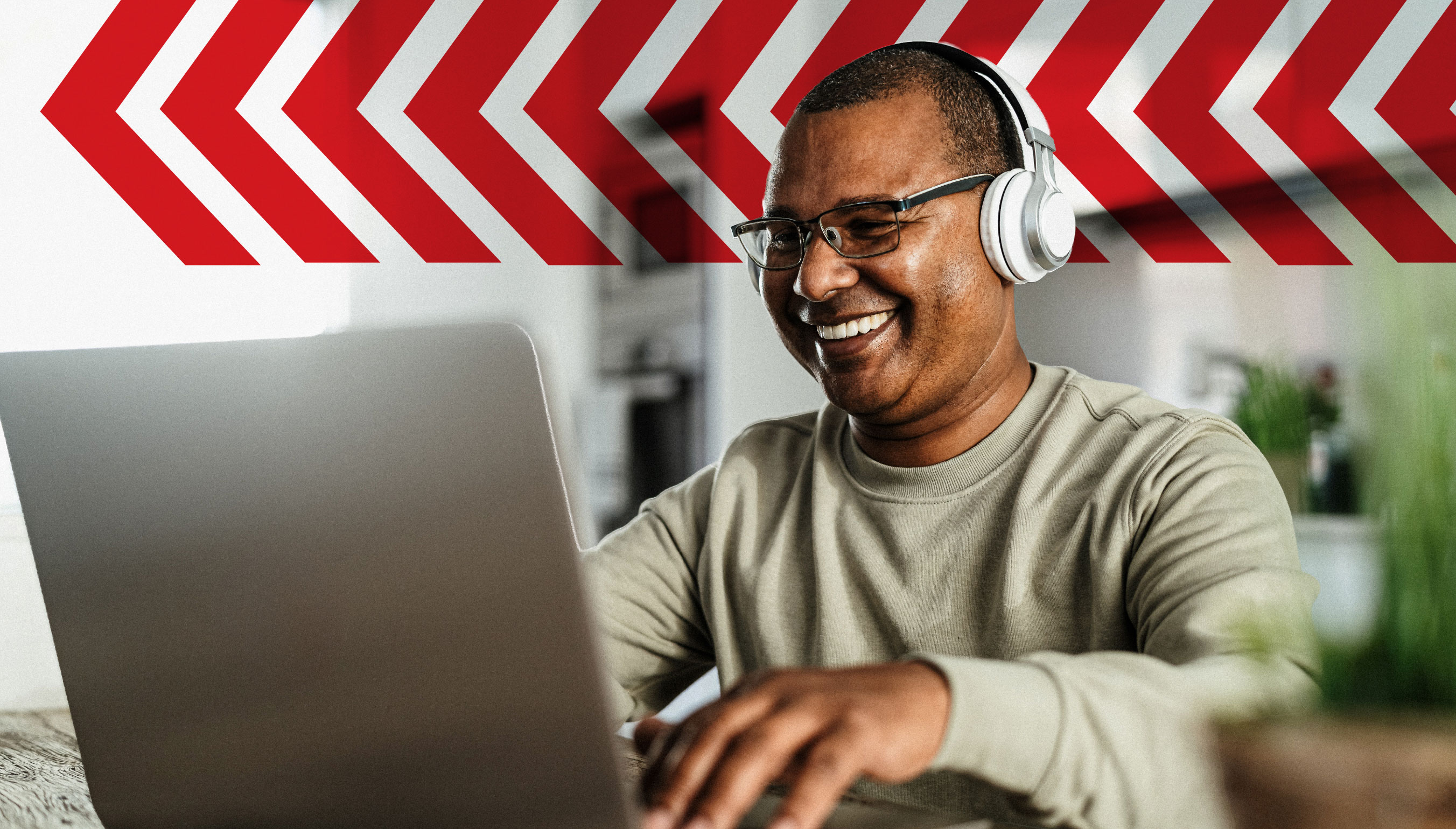 Smiling adult wearing headphones and glasses using a laptop at home, representing flexible online learning or remote education.